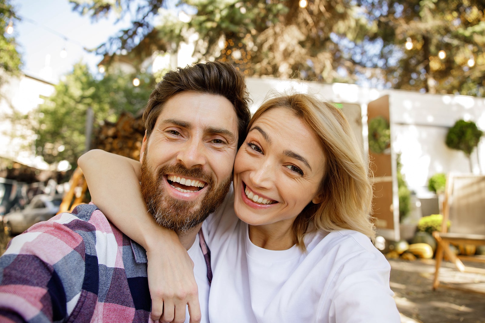A lovely couple are sitting near the travel trailer, taking a selfie, laughing having fun, enjoying their vacation. Portrait of in love enjoying a sunny day outside the city, camera view.