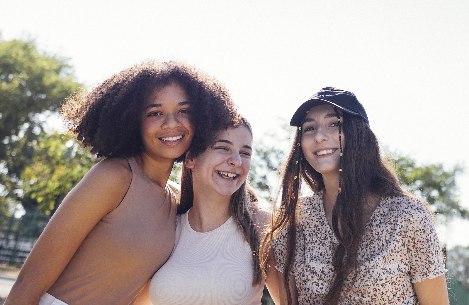 Group of teenagers of different nationalities and appearance have a fun together. Young and positive student girls in casual clothes with backpacks laugh and chat on the street. Friendship concept.