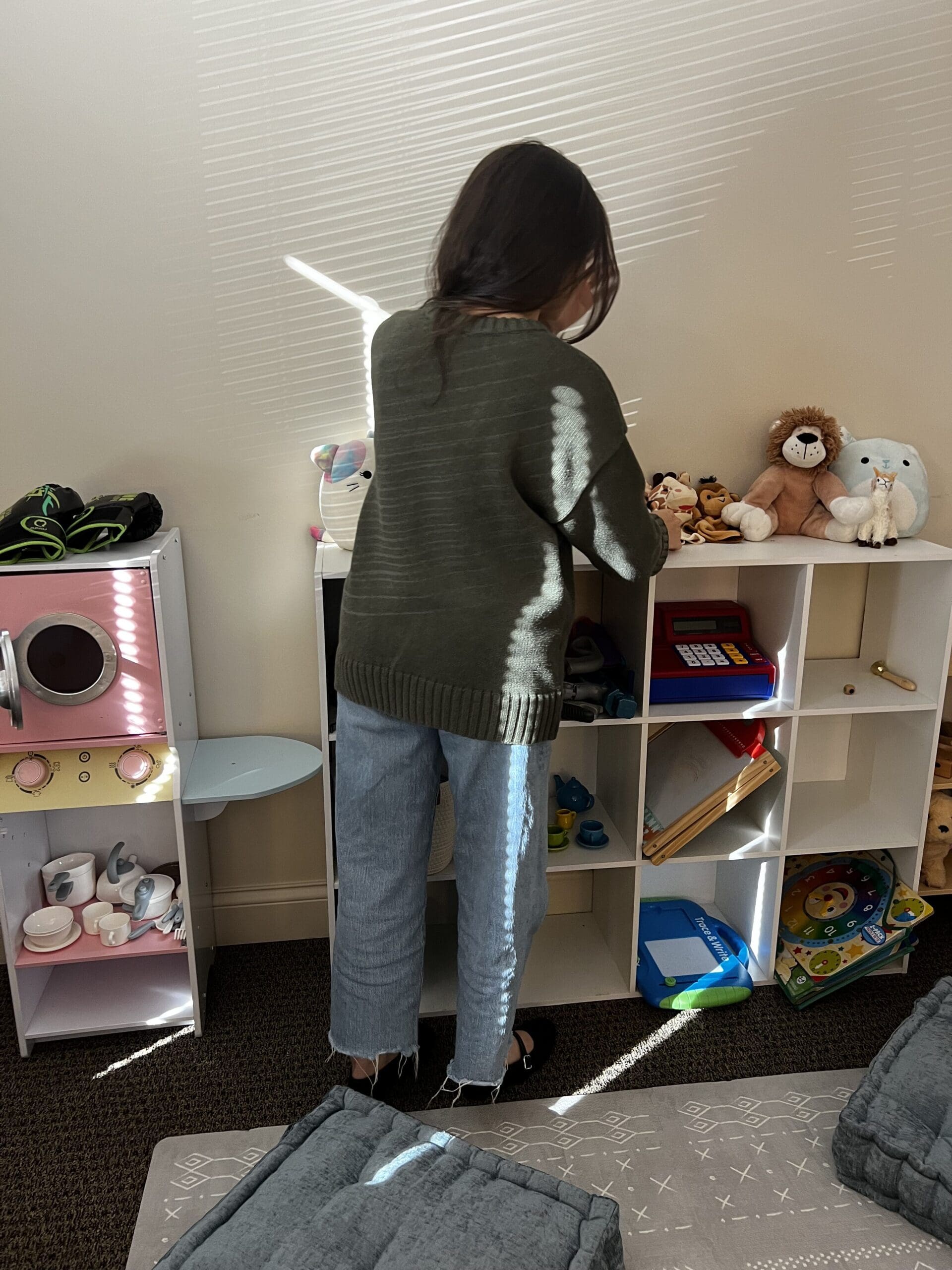 Therapist arranging toys and stuffed animals in a play therapy room, preparing a warm and supportive environment for child counseling and emotional development.