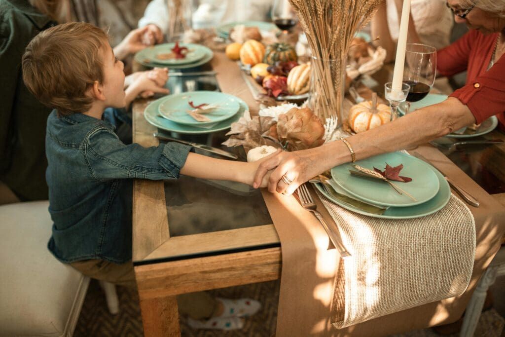 A young child holding hands with an older adult at a family table decorated for fall, representing connection, gratitude, and emotional warmth.