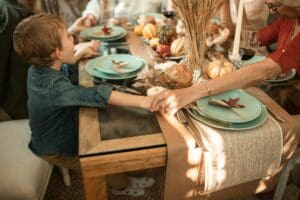 A young child holding hands with an older adult at a family table decorated for fall, representing connection, gratitude, and emotional warmth.