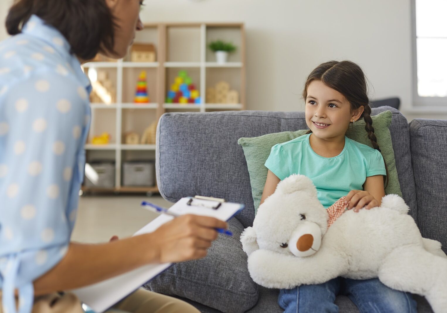 Cute little girl talking to child psychologist during therapy session in cozy modern office