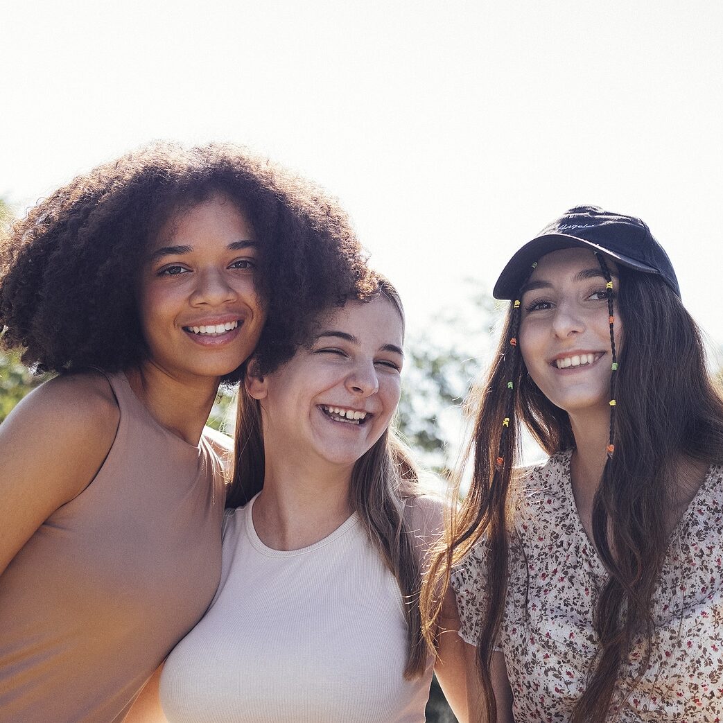 Group of teenagers of different nationalities and appearance have a fun together. Young and positive student girls in casual clothes with backpacks laugh and chat on the street. Friendship concept.
