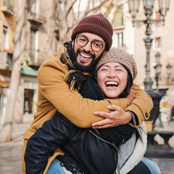 Young multiracial affectionate couple laughing and smiling together giving a piggyback ride, having fun embracing and hugging in a romantic date. Two friends bonding outdoors